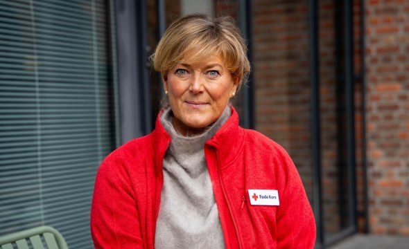 En kvinne med kort lyst hår og rød genser smiler mot kamera.