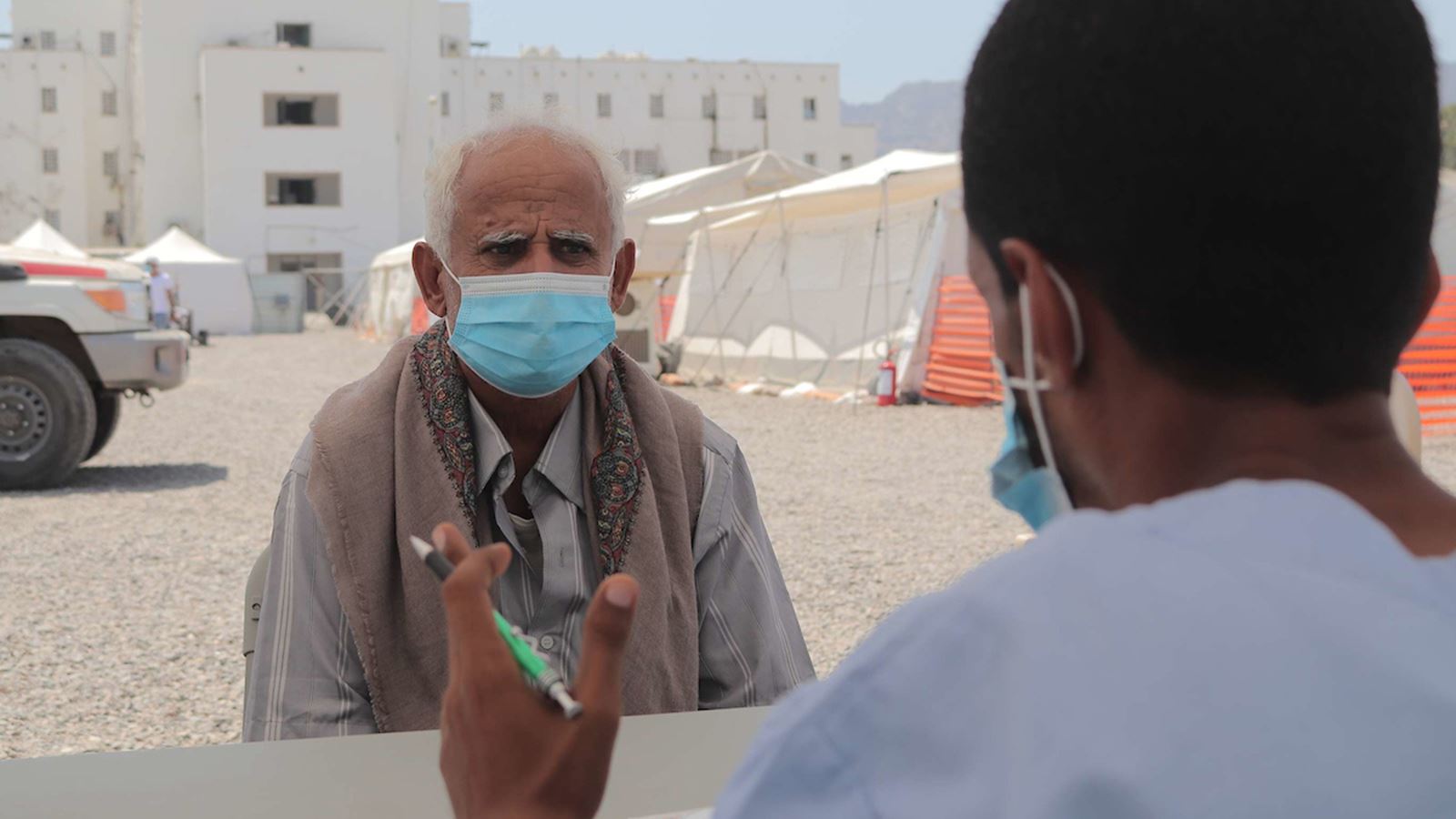 En eldre mann med munnbind snakker med en Røde Halvmåne ansatt. Aden Jemen