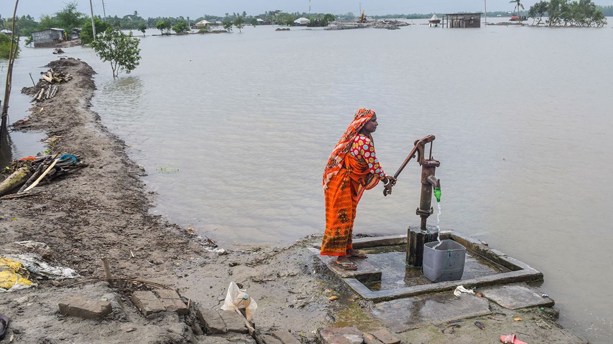 En enslig kvinne ikledd sari står ved elvebredden og pumper ogg skittent vann
