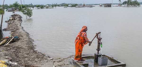 En enslig kvinne ikledd sari står ved elvebredden og pumper ogg skittent vann