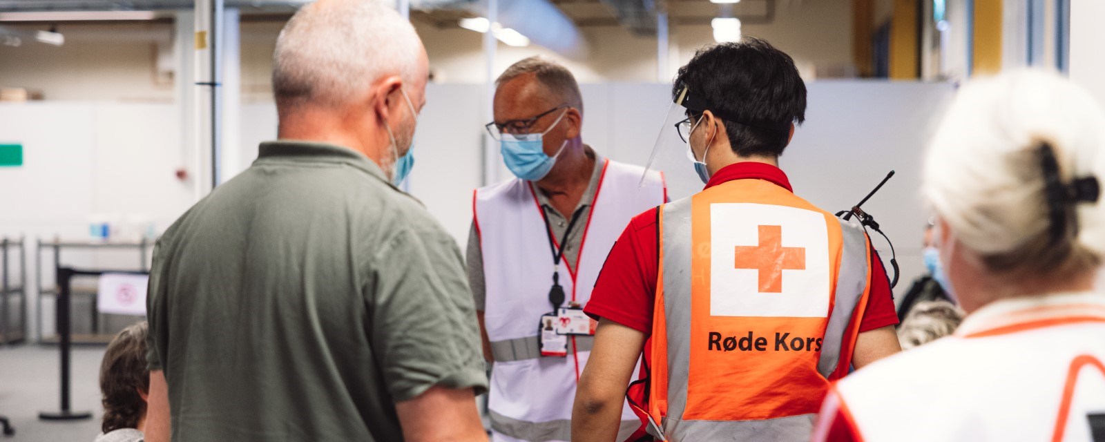 Tre frivillige fra Røde Kors snakker med en mann som skal ta vaksine