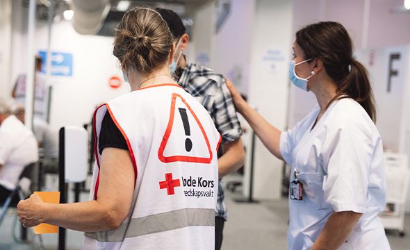 En kvinne fra Røde Kors snakker med en mann sammen med en kvinnelig sykepleier