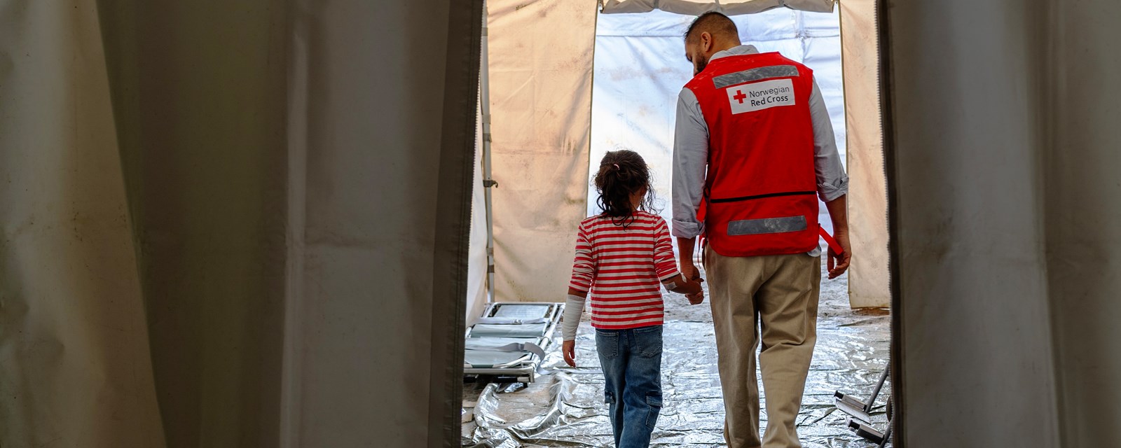 En lege fra Røde kors leier ei lita jente gjennom feltsyskehus
