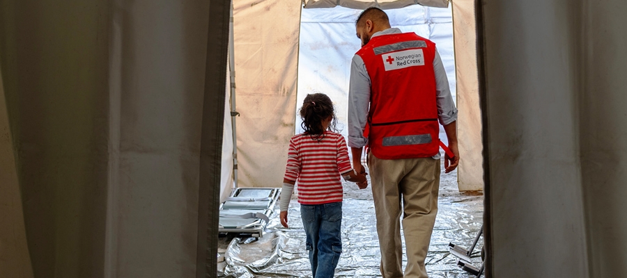 En lege fra Røde kors leier ei lita jente gjennom feltsyskehus