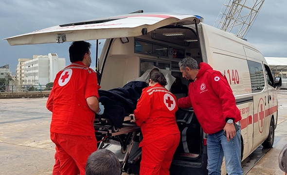 Tre Røde Korsere laster enn båre med en person inn i en ambulanse.