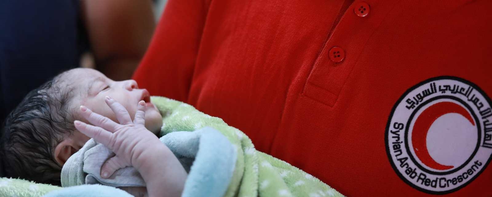 Nyfødte Aisha i armene til frivillig fra  Syria Røde Halvmåne.