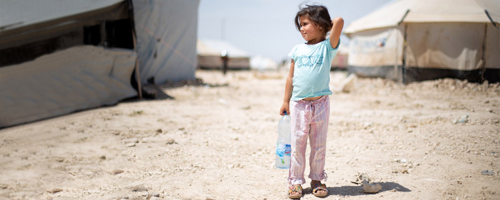 Jente står alene foran telt i flyktningleir