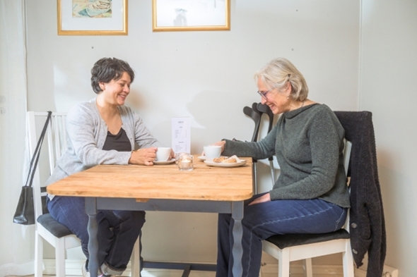 To glade kvinner sitter ved et bord og drikker kaffe sammen