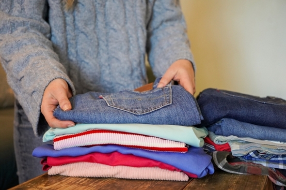 Hender som legger et plagg på toppen av en klesbunke