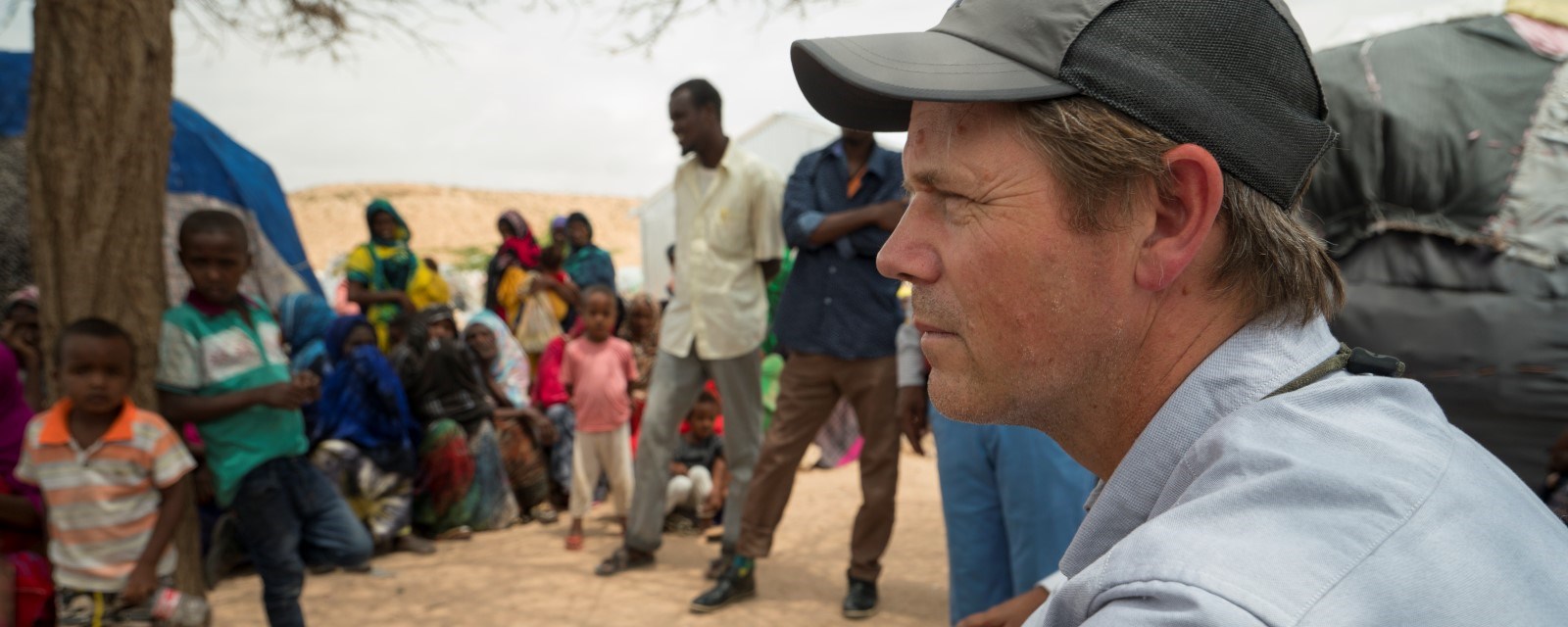 Bernt Apeland sitter i en landsby i Somalia, med barn som står rundt i en ring