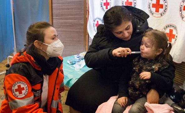 Mor og kvinner fra Røde Kors hjelper er lite barn