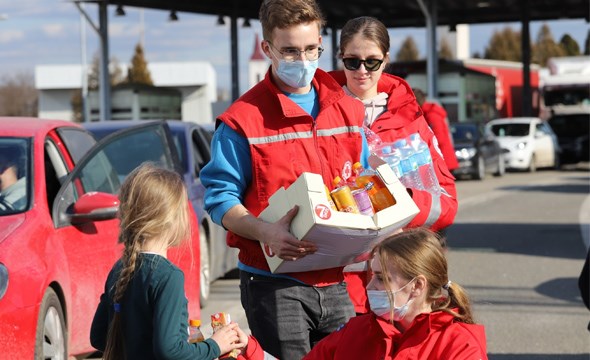 Frivillige i Røde Kors klær bærer mat og gir drikke til en liten jente