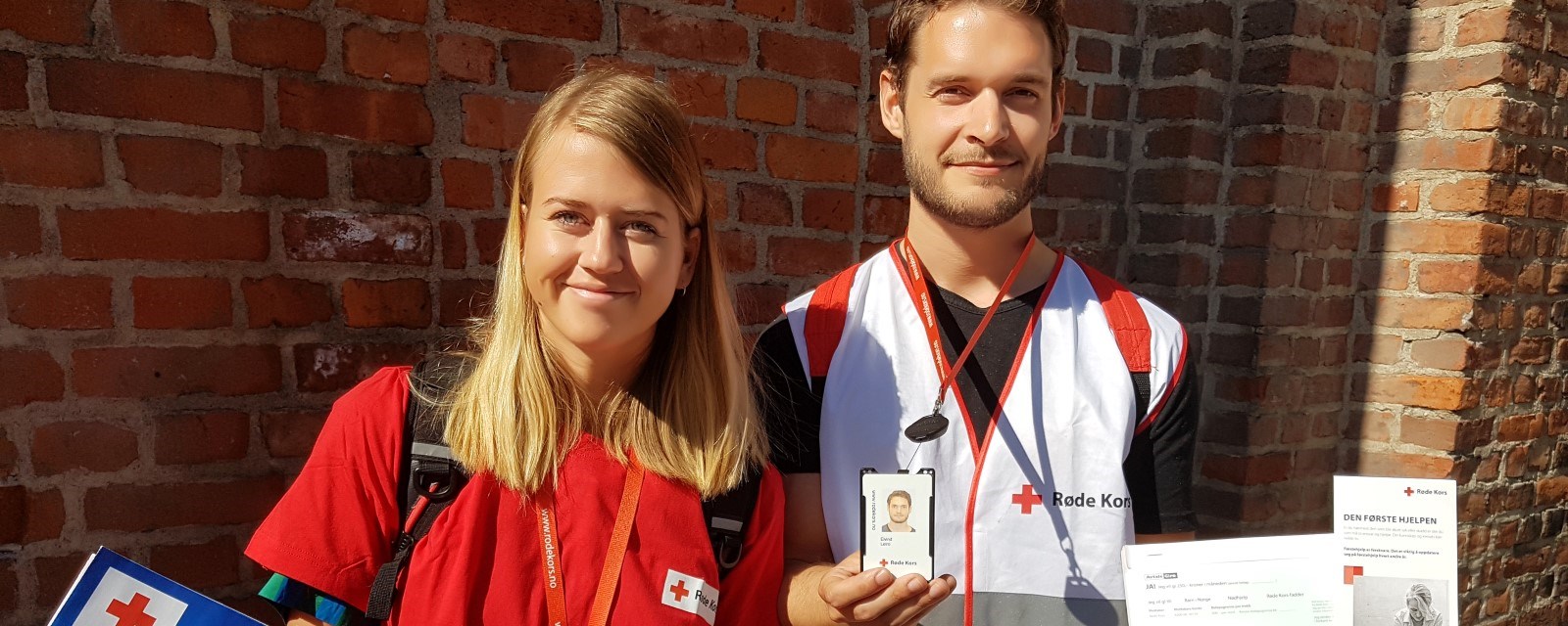 To norske ungdommer smiler til kamera, iført hvite Røde Kors-vester