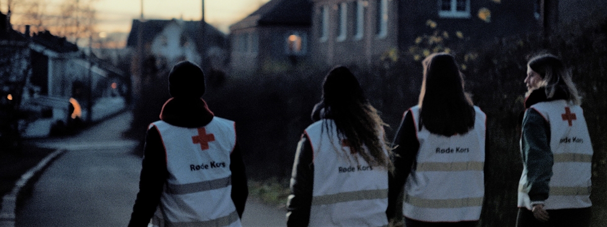 Fire personer, med ryggen til, går nedover en gate i skumringen.