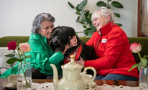 To eldre damer smiler sammen med en hund i fanget.