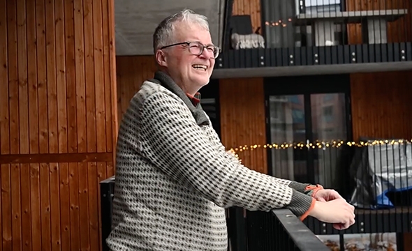 En mann i ullgenser står på en balkong og smiler.