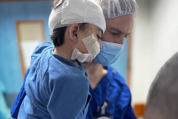 Et barn med bandasje blir båret av en lege med munnbind.