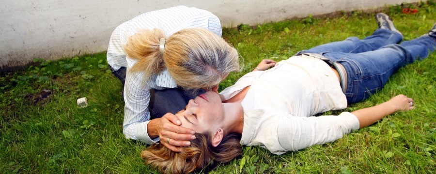 En kvinne bøyer seg ned og lytter til pusten på en kvinne som ligger livløs på bakken.