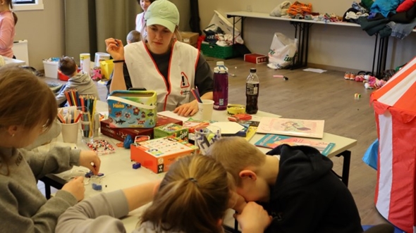 En frivillig sitter ved et lekebord med mange barn.