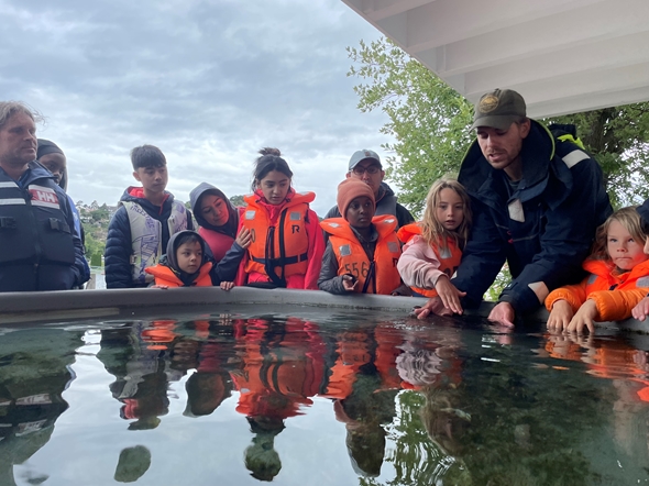Folkemenge med barn og voksne ikledd redningsvester foran et basseng.