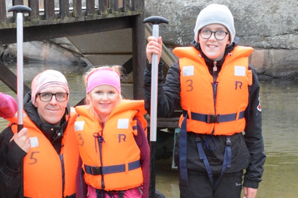 En voksen og to barn smiler til kamera med redningsvester på