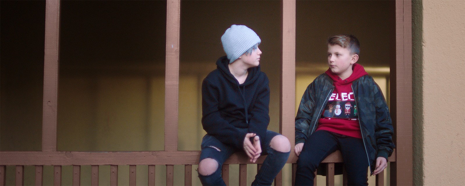 To unge gutter sitter på brunt tregjerde og snakker