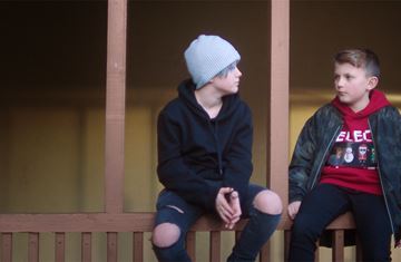 To unge gutter sitter på brunt tregjerde og snakker