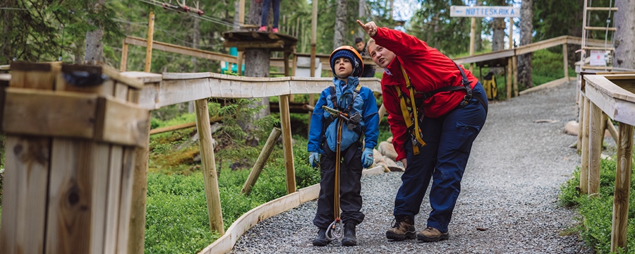 Liten gutt og voksen dame sammen i en klatrepark i skog.