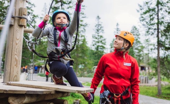 En dame hjelper en liten jente i en klatrepark.