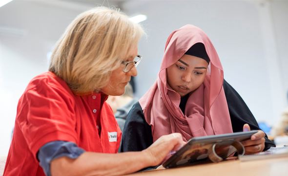 En voksen frivillig hjelper en yngre kvinne med lekser
