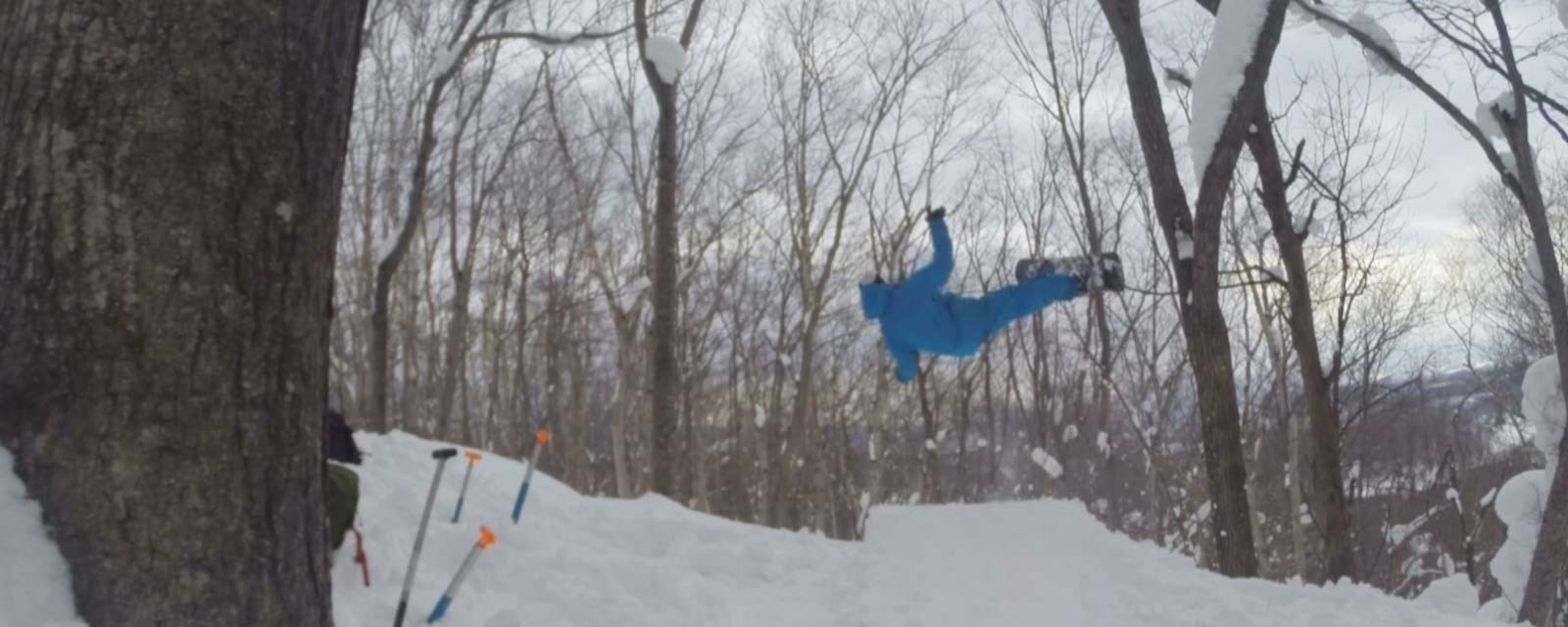 En snowboarder i blått antrekk tar av fra et hjemmelaget hopp i skogen
