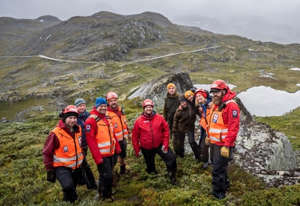 En gjeng med hjelpekorpsene i Røde Kors står på en høye med fjellandskap i bakgrunnen.