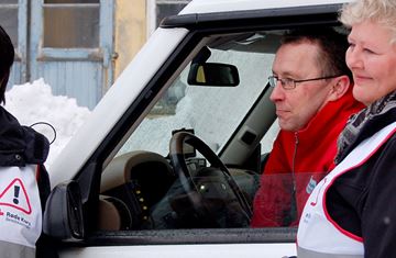 To voksne kvinner med hvite beredskapsvester står ved bil med mannlig kollega i rødekors fleece