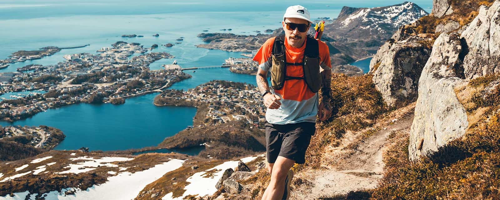 En mann i god form med treningsutstyr løper på fjellet. I bakgrunnen ser vi en vakker utsikt mot havet.