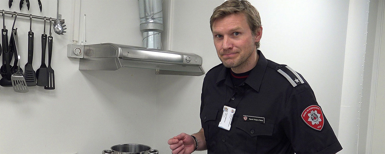 Branninnspektør står i et kjøkken og peker på kjøkkenvifta over komfyren