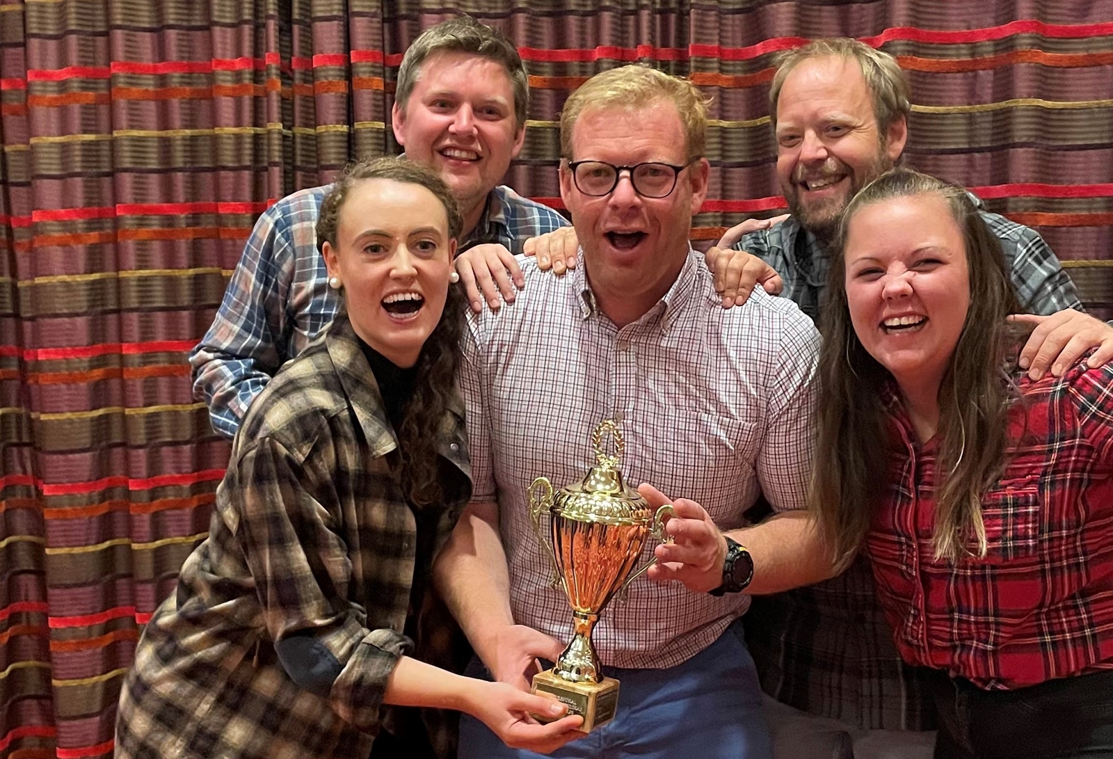 Fem jublende mennesker med en pokal.