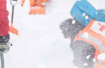 Fire hjelpekorpsere står på en snødekt fjelltopp og skuer ut i landskapet. 