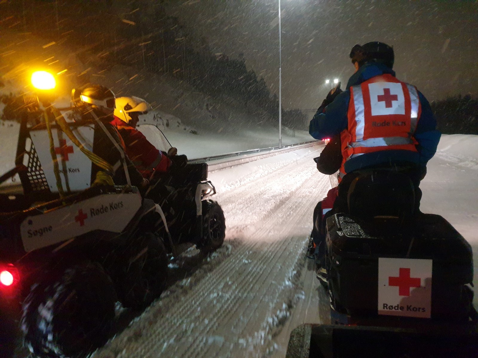 Snøscooter med mannskap fra Røde Kors kjører mellom lastebilder