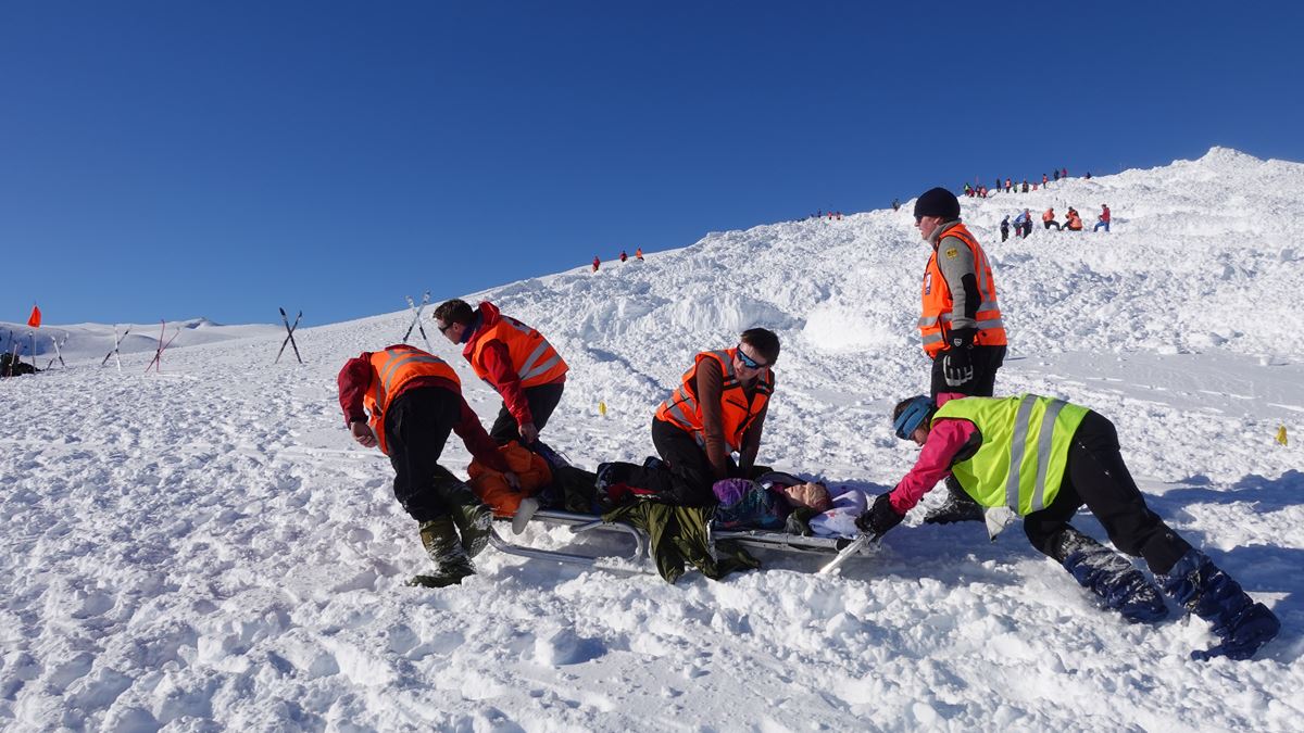 Person dras ut fra snøskred på en båre mens hjelpekorpser gjennomfører HLR.