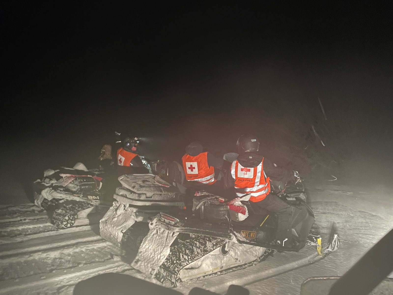 Hjelpekorpsere på snøscooter i fjellet på natten.