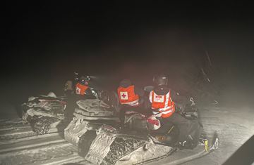 Hjelpekorpsere på snøscooter i fjellet på natten.