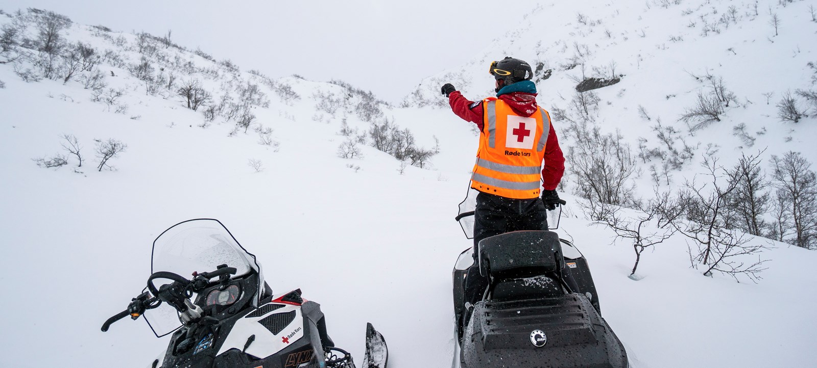 Røde Kors-frivillig på snøskuter i vinterfjellet.
