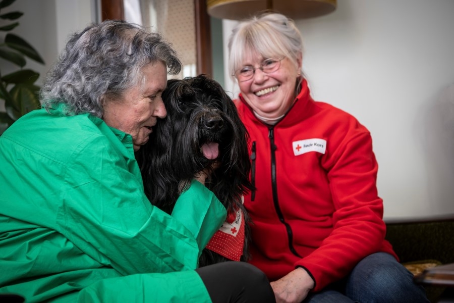 En eldre kvinne gir en klem til en svart hund.