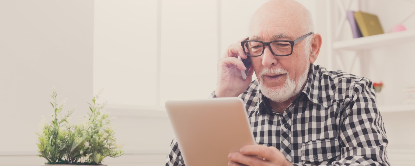 Eldre mann snakker i telefon samtidig som han ser på et nettbrett