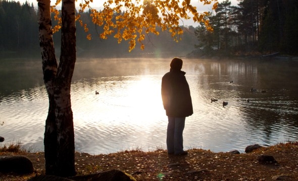 En person står med ryggen til og ser utover et lite vann.