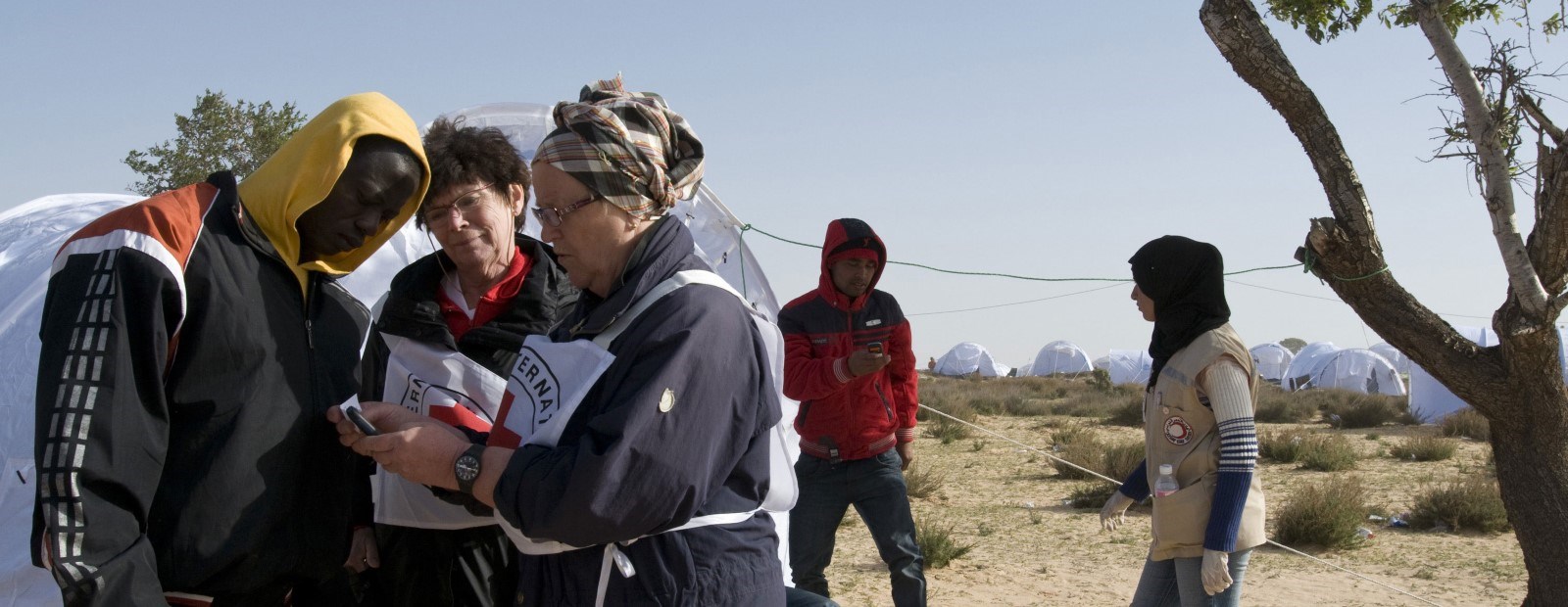 To kvinner fra internasjonale Røde Kors snakker med en yngre mann foran et telt
