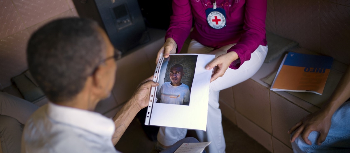 En mann ser på et bilde av en savnet person som en frivillig i Røde Kors holder opp.