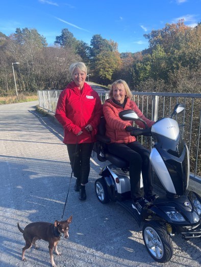 Besøksvenn Monica er ute på tur med hunden Knerten og sin besøksvert Reidun. Hun kjører en elektrisk rullestol.