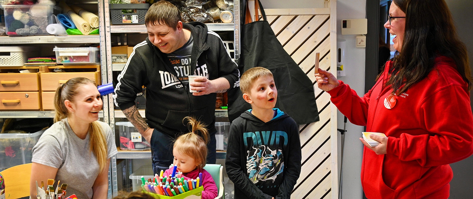 Barn og voksne i muntert samspill med Røde Kors frivillig