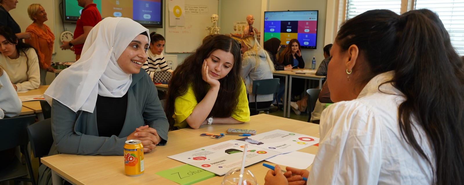 Tre jenter sitter rundt en pult i et klasserom